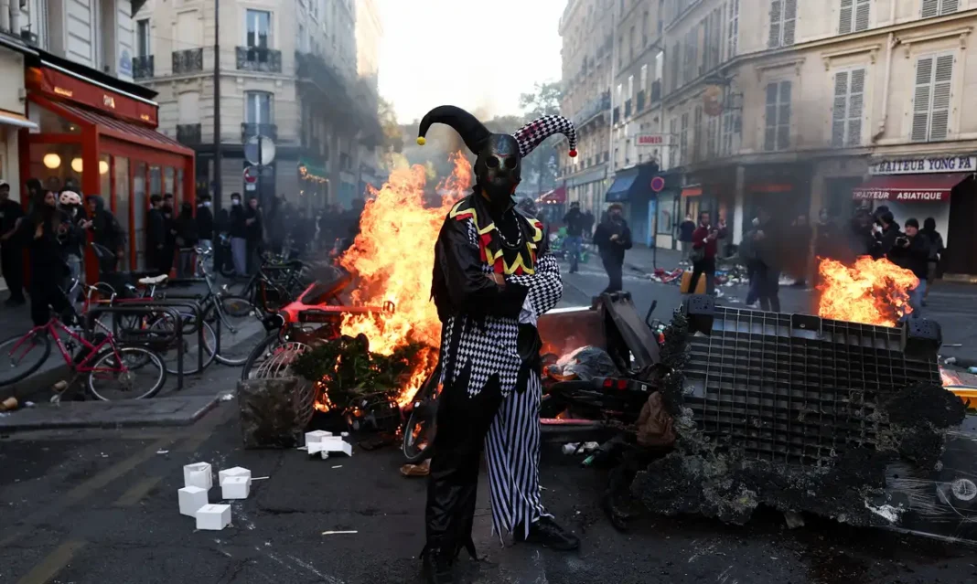França quer impor toques de recolher após fim de semana com tumultos A demonstrator wearing a costume stands in front of burning flames, in Paris, France, October 18, 2026. REUTERS/Abdul Saboor